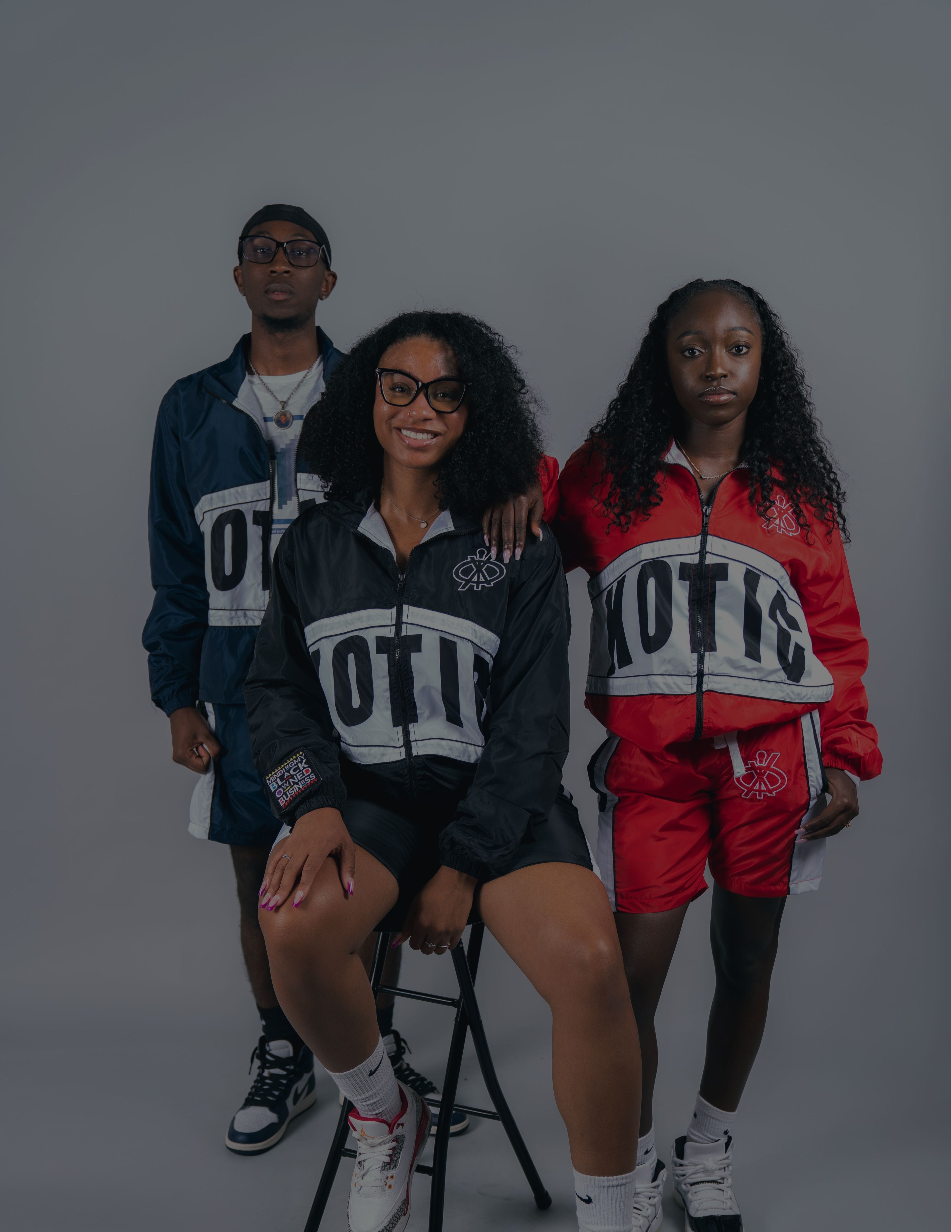 Three people wearing matching tracksuits with 'XOTIC' branding on a gray background